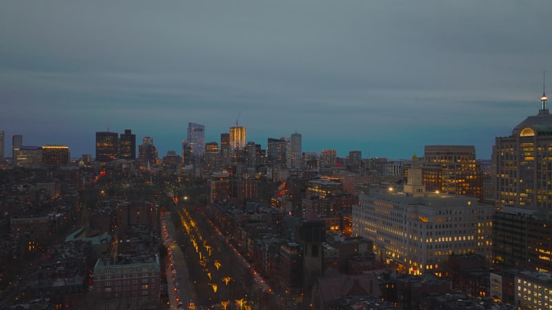 Fly above evening city. Illuminated streets and lighted windows in buildings. Aerial view of urban neighbourhood. Boston, USA