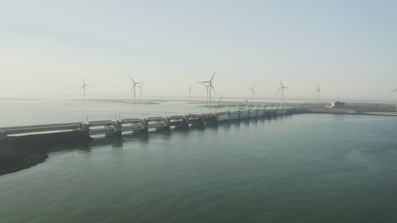 Stunning aerial view of the offshore wind turbine field with storm barrier bridge in the front.