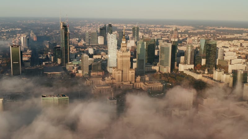 Aerial panoramic footage of downtown high rise buildings in morning sun. Historic PKIN buildings and modern office skyscrapers above fog. Warsaw, Poland