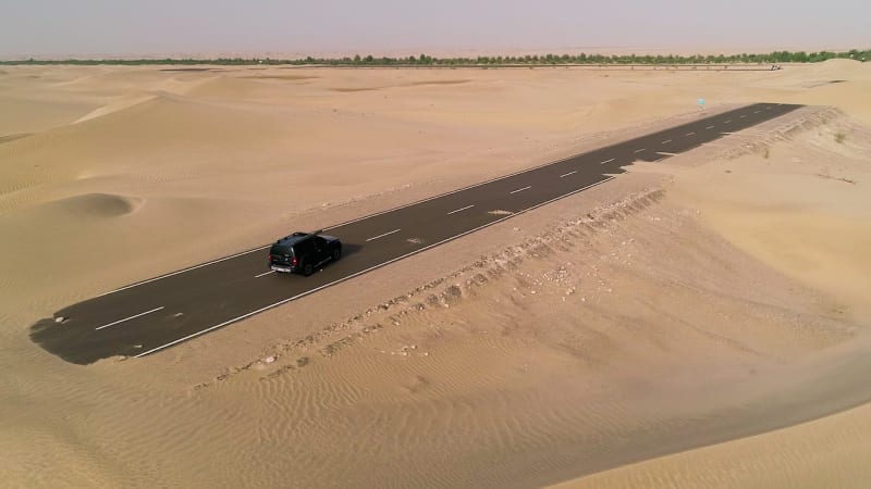 Aerial view of black car driving on road covered by sand.