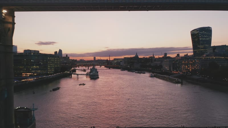 Backwards reveal of famous Tower Bridge against twilight sky. Cars driving on bridge across River Thames. London, UK