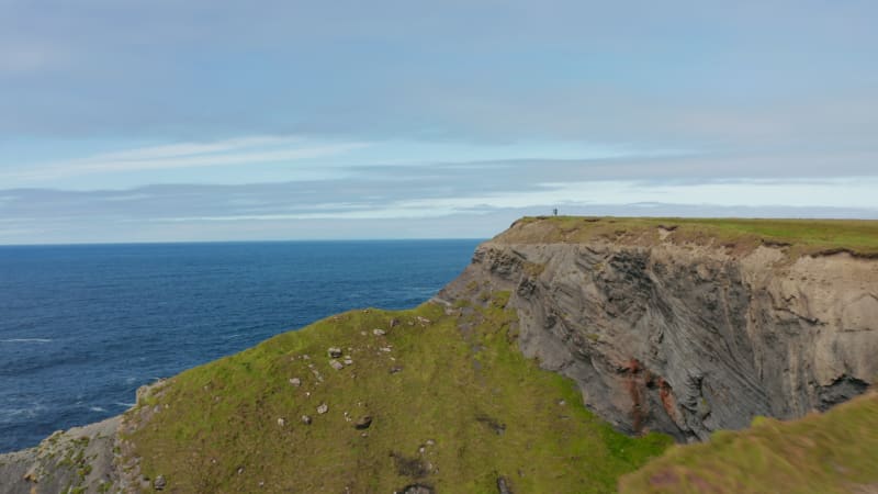 Forwards fly above sea coast. High rocky cliffs steeply falling to sea. Revealing waves crashing to coast. Kilkee Cliff Walk, Ireland