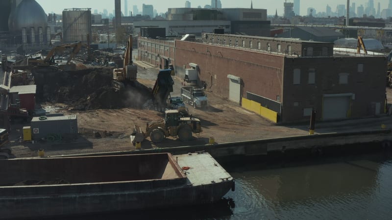 Trucks bringing loose material to transhipment point in industrial site. Dumping load on ground. New York City, USA