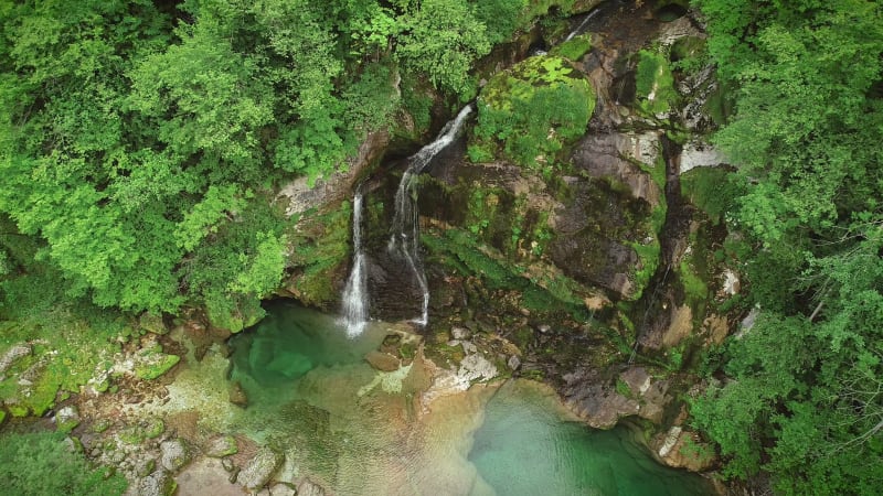 Aerial view of the top of a small waterfall with clean water downhill.