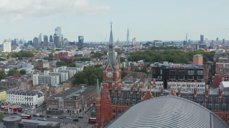 Aerial panoramic view with red brick clock tower in foreground and modern tall skyscrapers in background. London, UK
