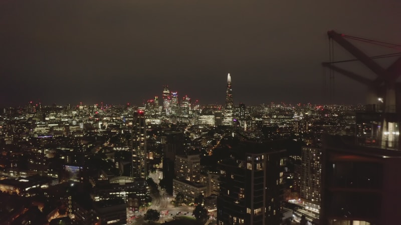 Forwards fly around tall apartment buildings. Revealing night cityscape with glowing downtown skyscrapers. London, UK