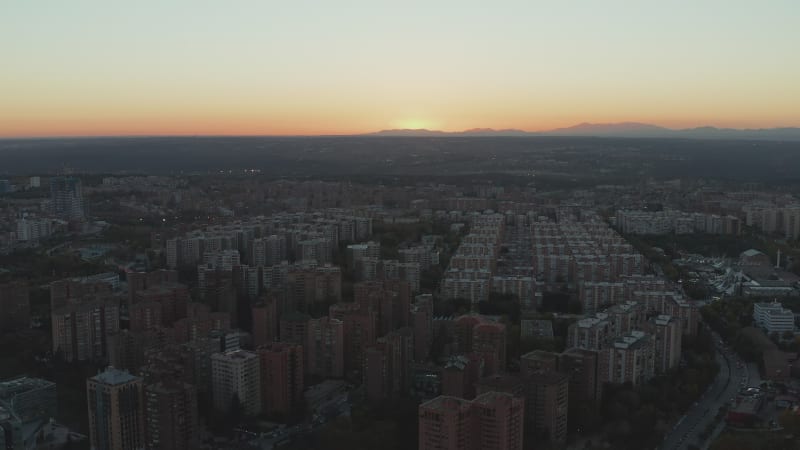 Aerial view of apartment houses on vast housing estate in town at dusk. Sun setting behind mountain ridge in distance.