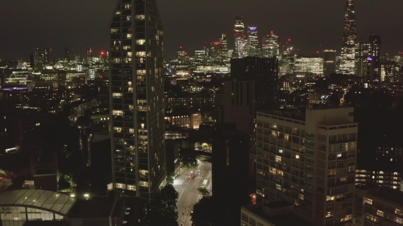 Tilt up reveal of downtown skyscrapers at night. Aerial view of street leading between apartment buildings. London, UK