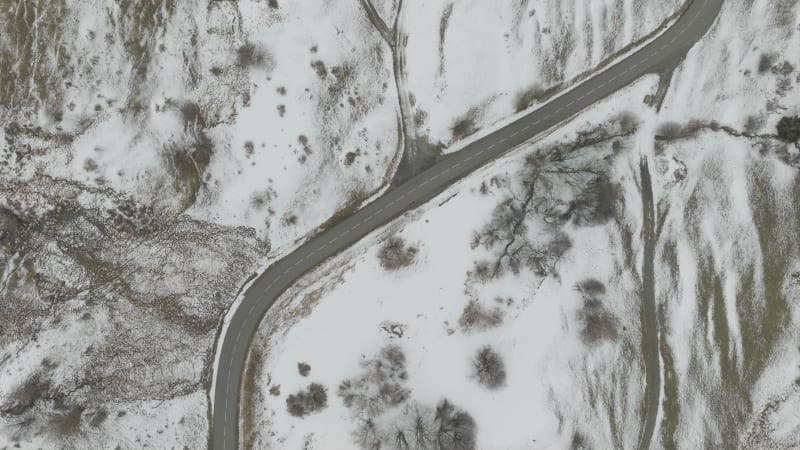 Forwards top down shot of an empty curved mountain road in snow covered landscape in Les Sybelles, France in cloudy weather.