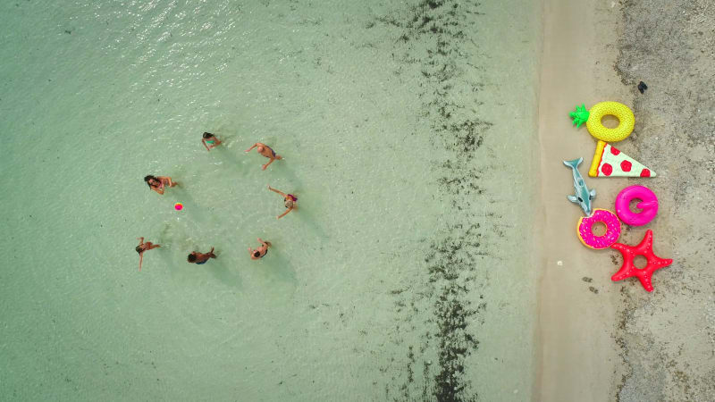 Aerial view of group of friends playing volleyball in sea by sandy beach.