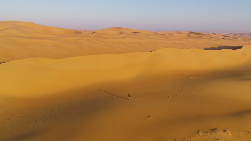 Aerial view of a man walking on dunes during the sunset.