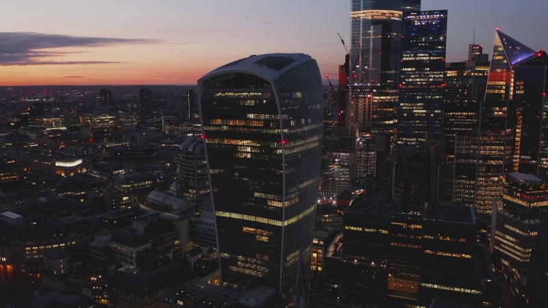 Slide and pan footage of modern futuristic office buildings in City financial hub after sunset. Iconic Walkie Talkie skyscraper with Sky Garden under roof against twilight sky. London, UK