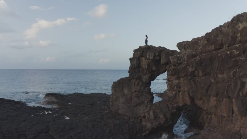 Aerial view of a person standing alone on top of a natural arch along the coastline, Mauritius island.