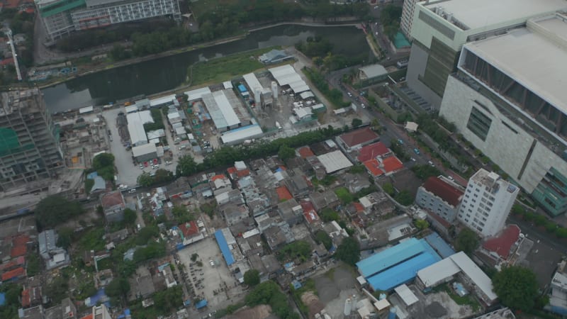 Aerial tilting view into overhead shot of dense urban neighborhood surrounded by tall skyscrapers in Jakarta, Indonesia