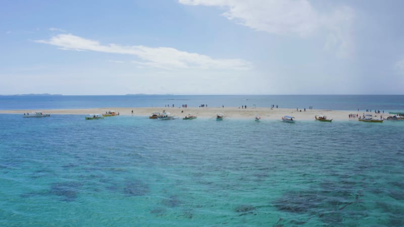 Sandbar in serene crystal water with tourists and bangka boats