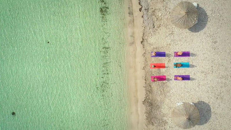 Aerial view of yoga group on mats on beach with parasols.