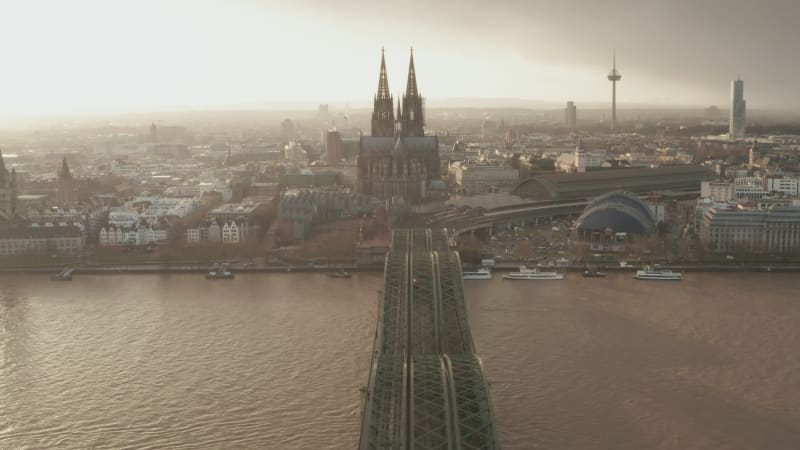 Forwards fly above railway bridge over wide river. Silhouette of two towers of Cologne Cathedral against glowing sunset sky. Cologne, Germany