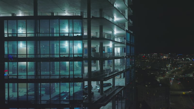 Descending shot along brightly illuminated construction site of modern high rise building at night. Boston, USA