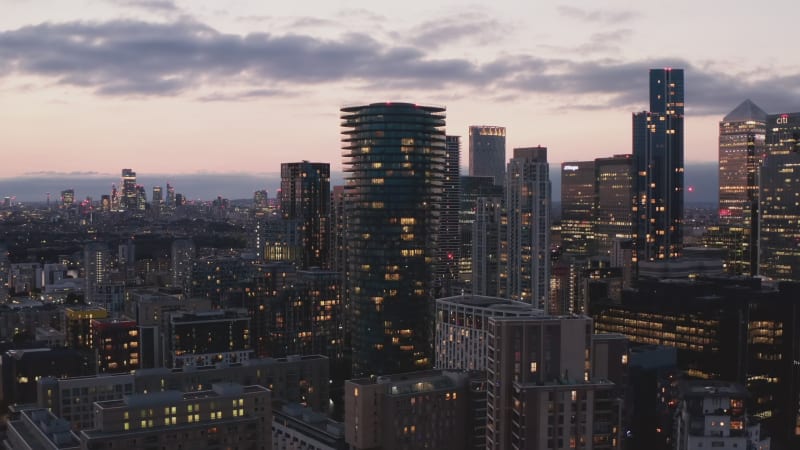 Panorama curve shot of modern business urban district with tall skyscrapers in blue hour. Cityscape against pink twilight sky. London, UK