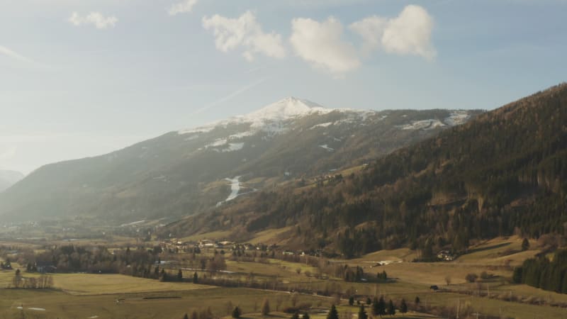 Pullback shot through wide valley with snowy mountain peak