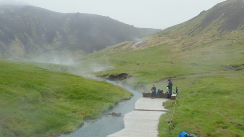 Drone view of Reykjadalur hot thermal river flowing through valley in Iceland. Aerial view of natural geothermal hot river stream in Reykjadalur Valley with wooden footpath and changing rooms