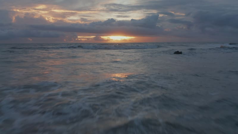 Low aerial shot of rough sea waves  during golden sunset in Bali. Point of view of ocean waves crashing ashore in beautiful warm evening light