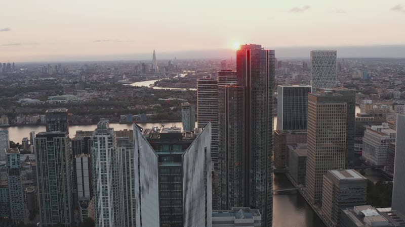 Modern skyscrapers in Canary Wharf district. Forwards fly above Isle of Dogs against setting sun. London, UK