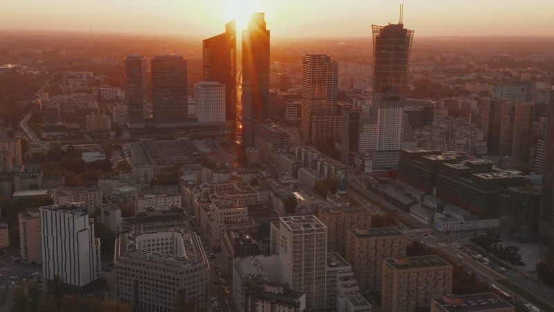 Fly above large city. Tilt up reveal downtown skyscrapers against bright sunset light. Warsaw, Poland