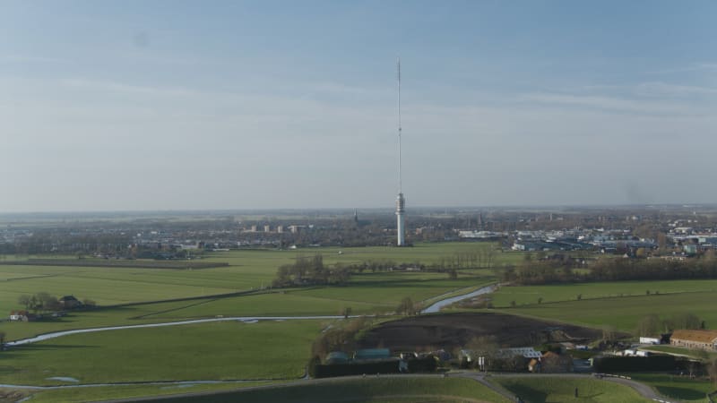 Lopik tower in distance in the middle of agricultural land with villages in front and behind where there are moving vehicles and flying birds