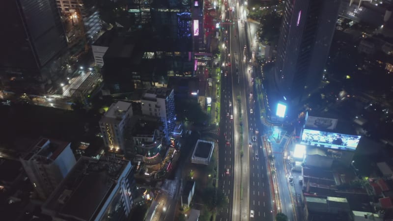 Tilting aerial shot flying towards cars on a highway at night in busy urban metropolitan city center of Jakarta