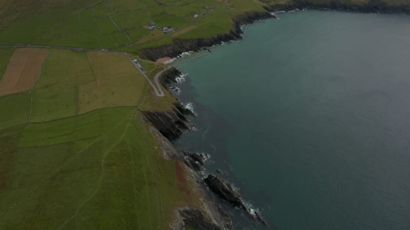 High angle footage of steep and high escarpments falling to water. Green pastures along rugged sea coast. Ireland