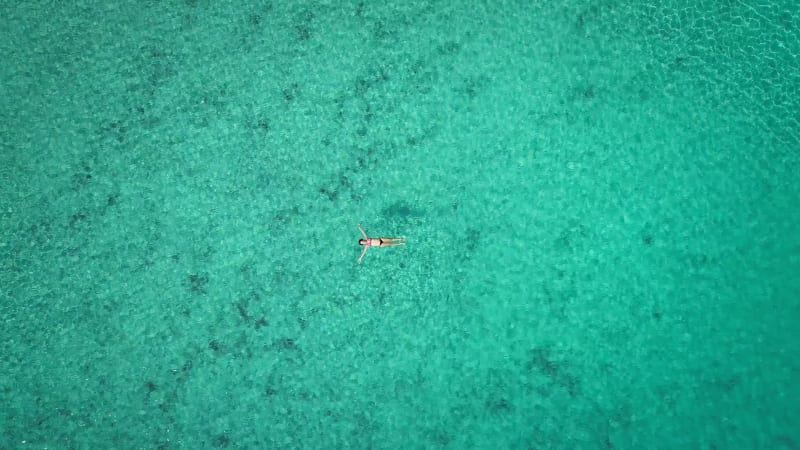 Zoom out aerial view of pregnant woman floating on her back