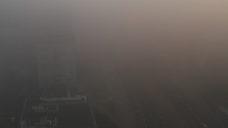 Forwards fly above wide street. Road gradually hiding into dense fog. Misty morning in city. Warsaw, Poland