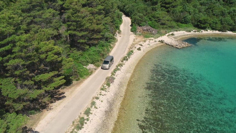 Aerial view of campervan driving near turquoise water