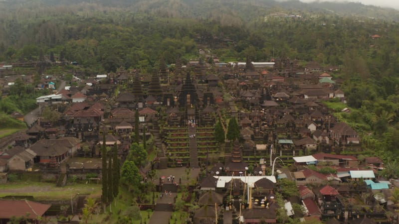 Aerial dolly view of tourists exploring the Besakih Temple in Bali, Indonesia. People at the famous tourist destination viewing the religious buildings and structures in famous Hindu temple