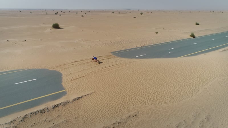 Aerial view of woman doing exercise in road cover by sand on Abu Dhabi