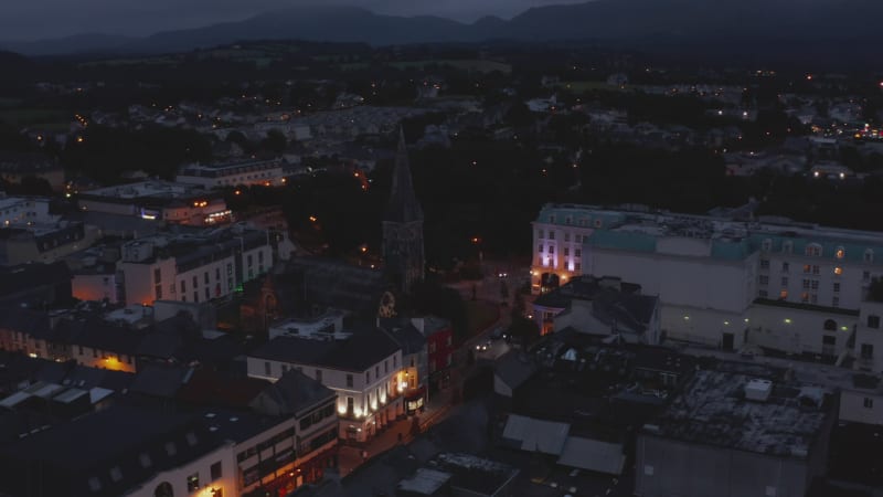 Aerial shot of medieval church in town centre. Illuminated colour houses facades in evening. Killarney, Ireland