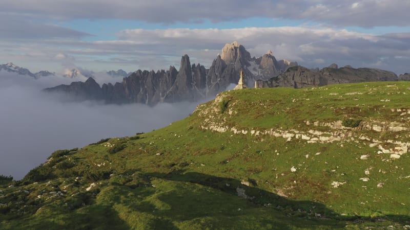 Aerial view of road through green Summer meadows towards rugged mountain range in the Dolomites