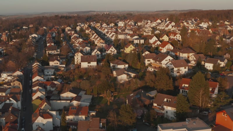 Forward flying drone over streets with family houses in evening light. Tilting up and heading to detail of several houses. Aerial view. Bad Vilbel, Germany.