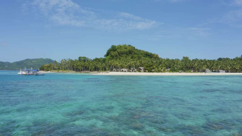 Low flying shot over crystal blue water approaching a tree covered island