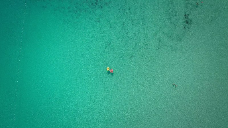 Aerial abstract view of two people floating in open sea on inflatables.