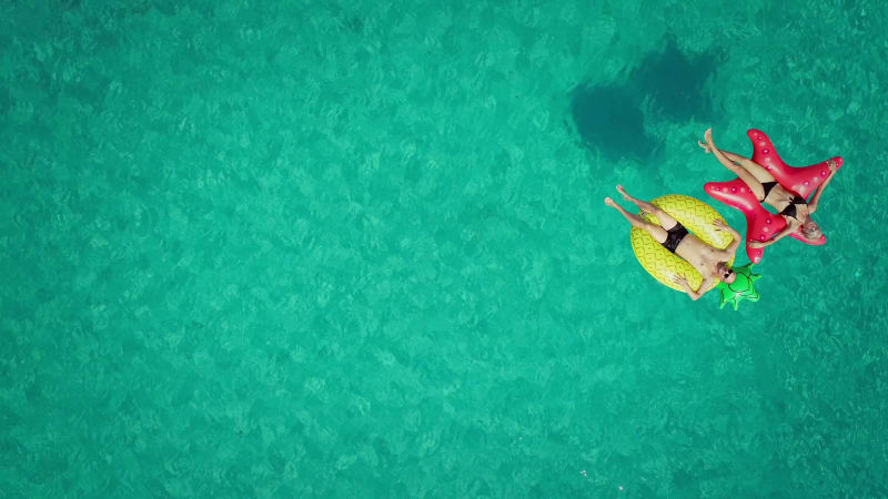 Aerial view of man and woman floating by string buoy on inflatable mattresses.