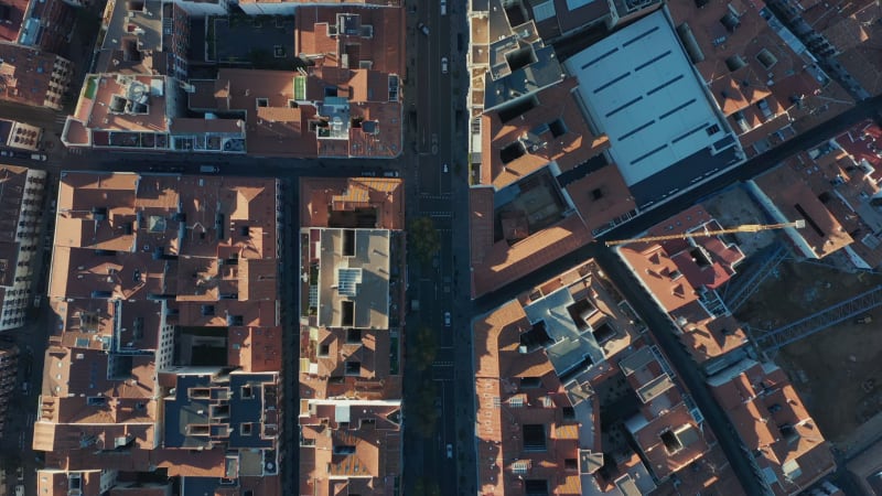 Aerial birds eye overhead top down panning shot of blocks of buildings in town. Tracking of vehicles driving in streets.