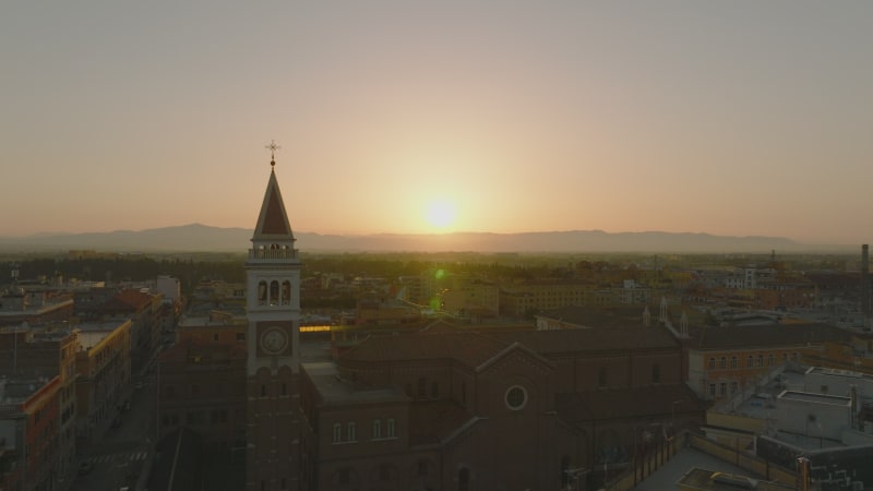 Aerial view of church and square tower against sunrise sky. Backwards reveal of buildings in city centre. Rome, Italy