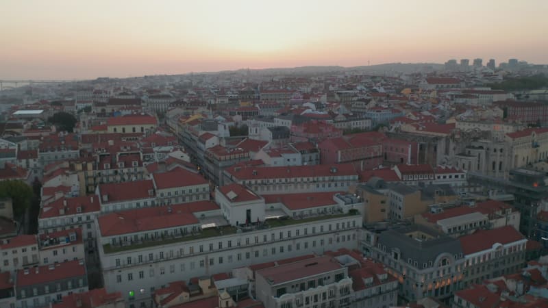 Aerial view of colorful rooftops of traditional old houses in Lisbon city center with reveal of Ponte 25 de Abril red bridge in the background