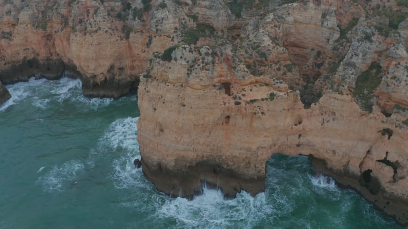 Aerial drone tilt down above rocky cliff coast in Lagos, Algarve, Portugal, birds eye overhead top down, windy day