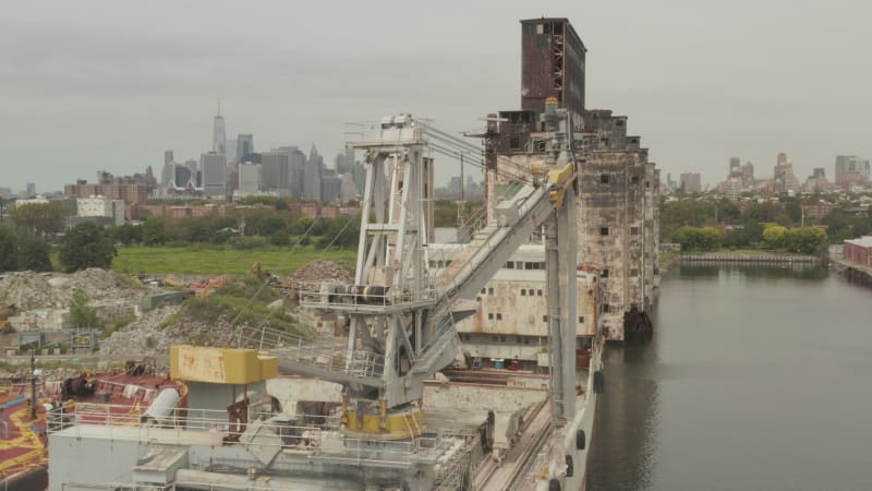 Close up of old rusty Cargo Ship Crane and Warehouse with New York City Skyline in background on a Cloudy Grey day