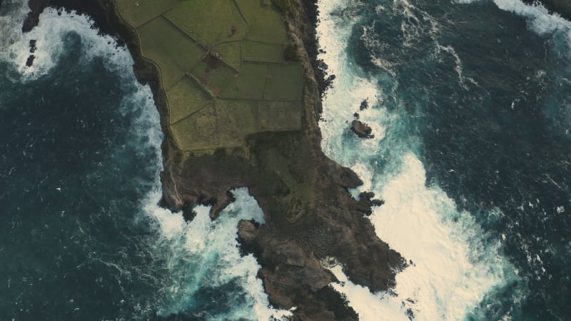 Aerial view of the crispy waves breaking on the rocks.