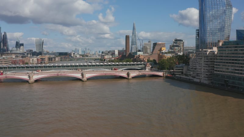 Forwards ascending fly above River Thames. Gradually revealing bridges across water and various buildings on both banks. Sunny day in city. London, UK