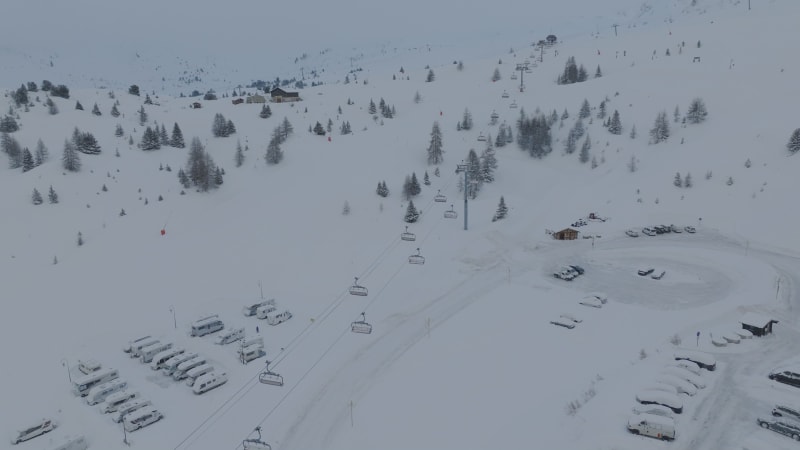 Flying over snow-covered cars, chair ski lift, snow covered trees at La Plagne, France at snowing misty morning